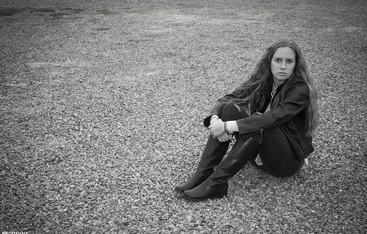 Young adult female model sitting on gravel road