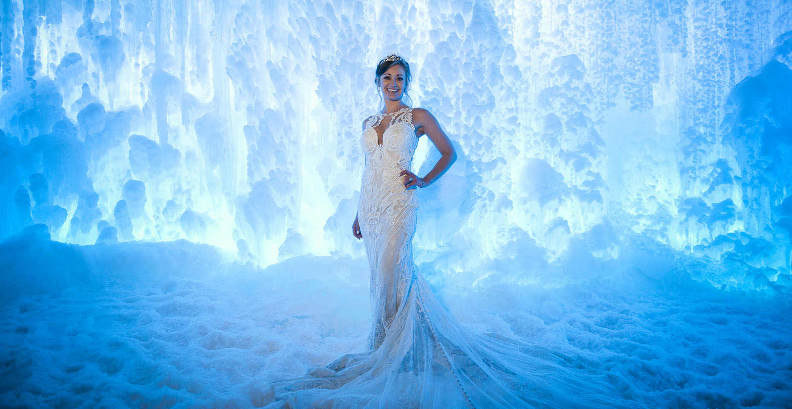 Beautiful bride in wedding gown standing in front of a blue ice wall at night, in Dillon, CO