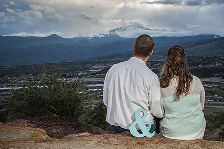 the backs of an engaged couple looking up at Pikes Peak