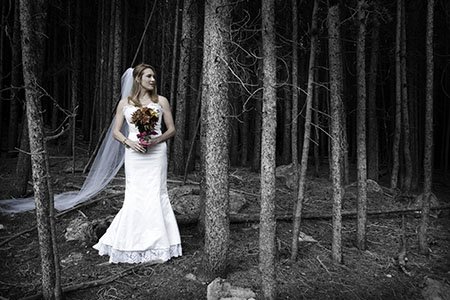 Bride in gown and bouquet standing in the woods of Colorado