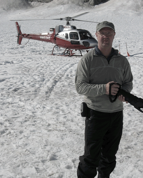 Brody standing in front of a helicopter in the snow, taking photos of a corporate event in Alaska